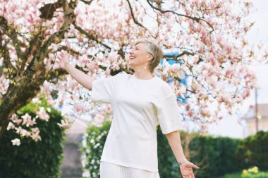 55-60 yaşındaki güzel bir kadının manolya ağacıyla poz verdiği bahar portresi.