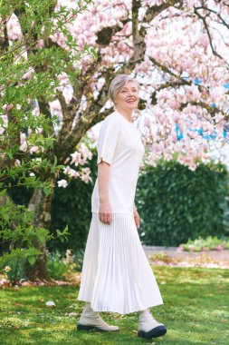 55-60 yaşlarında manolya ağacıyla poz veren güzel bir kadının tam bahar portresi.