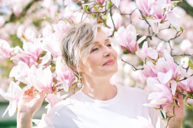 55-60 yaşındaki güzel bir kadının manolya ağacıyla poz verdiği bahar portresi.