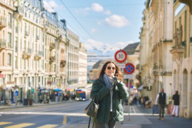 Şehir arka planında poz veren mutlu orta yaşlı kadın portresi, kalın kıyafetler giyiyor.