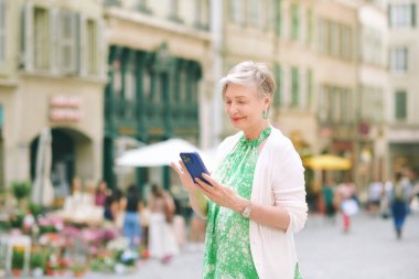 Şehir arka planında poz veren 55-60 yaşlarında güzel bir kadının açık hava portresi.