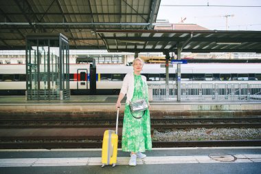 55-60 yaşlarındaki bir kadının tren istasyonundaki açık hava portresi. Tatil ve aktif yaşam tarzı. Fotoğraf İsviçre, Lozan 'da çekildi.