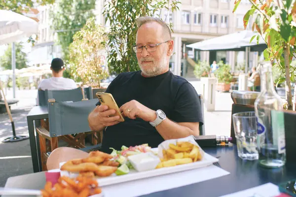  Restoranda rahatlayan, cep telefonu kullanan orta yaşlı bir adamın açık hava portresi.