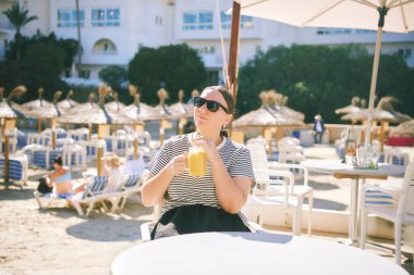 Sahildeki kafede bir bardak smoothie, rahatlama ve tatil yaşam tarzıyla dinlenen mutlu orta yaşlı kadının açık hava portresi.