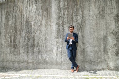 Dışarıda çalış. Gri duvarın yanında takım elbiseli bir adam duruyor.