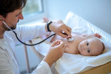Kalp ritmi. Erkek çocuk doktoru steteskopla bebeğin kalbini dinliyor.