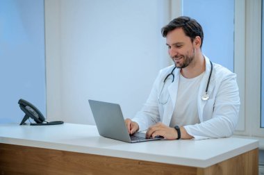 İşteki doktor. Koyu saçlı, sakallı genç doktor hastanedeki iş yerinde.