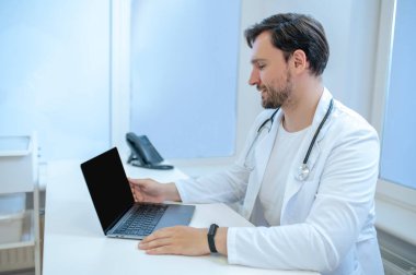 İşteki doktor. Koyu saçlı, sakallı genç doktor hastanedeki iş yerinde.