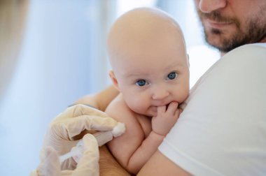 Steril eldivenli bir çocuk doktoru tek kullanımlık şırınga kullanarak yeni doğmuş bir bebeğe kas içi enjeksiyon uyguluyor.