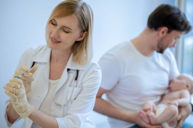 Steril eldivenli gülümseyen çocuk doktoru ilacı şırınganın içinden çıkarıyor.