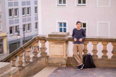 Gülümseyen mutlu bir çocuğun uzun bir portresi beton balyalara yaslanmış ve başka yöne bakıyor.