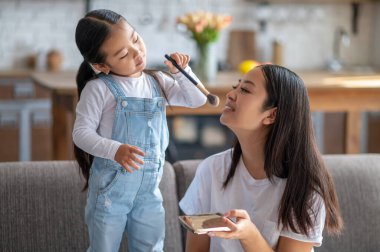 Annesi elinde pudra kutusuyla kanepede otururken kızı yüzünü pudralıyordu.