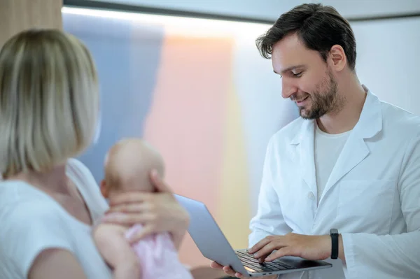 Focado Jovem Médico Digitando Seu Laptop Frente Uma Mulher Bebê — Fotografia de Stock