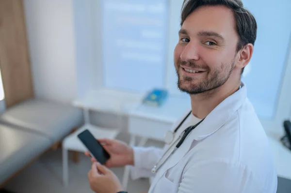 Portret Wesołego Lekarza Pozującego Aparatu Smartfonem Rękach — Zdjęcie stockowe