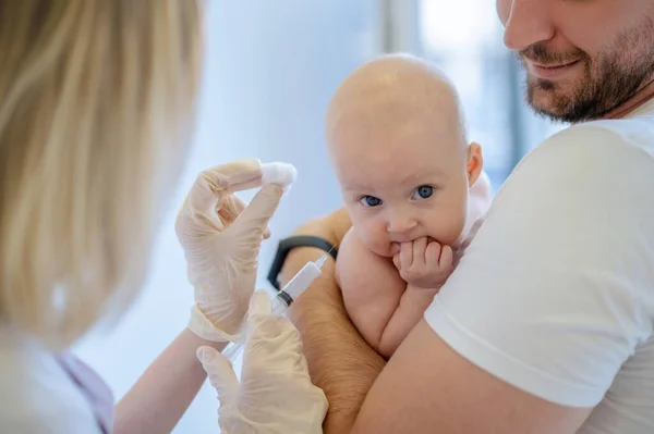 stock image Healthcare worker showing a disposable syringe to a cute calm baby held in father arms