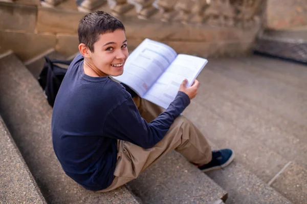Elinde Açık Bir Kitapla Beton Merdivenlerde Oturan Neşeli Genç — Stok fotoğraf