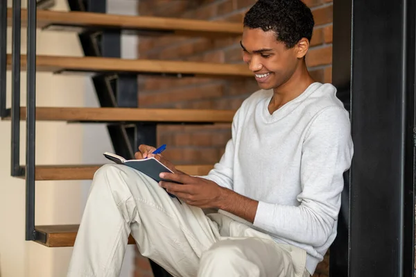 做笔记 身穿白衣的年轻人坐在木制楼梯上做笔记 — 图库照片