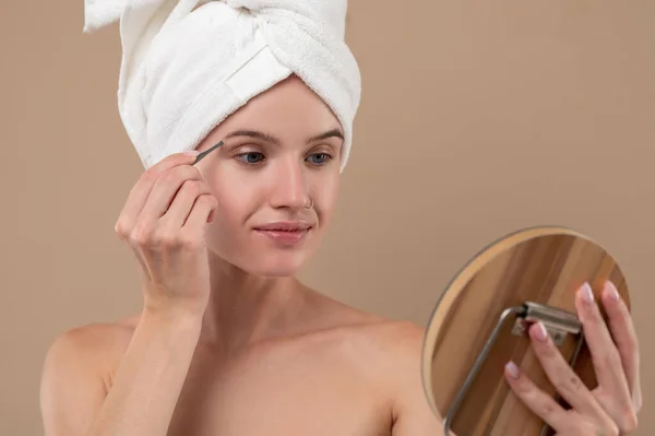Beauty tricks. Young girl with towel on head making eyebrows