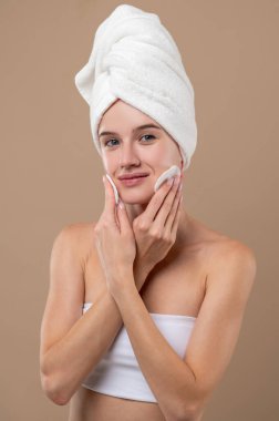 Yüz bakımı. Genç kız sakin görünüyor ve yüzünü temizliyor.