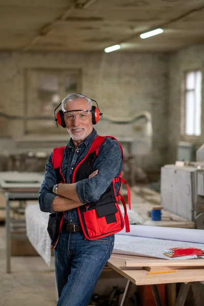 In a workshop. Mature man in eyeglasses and ear protector in a workshop