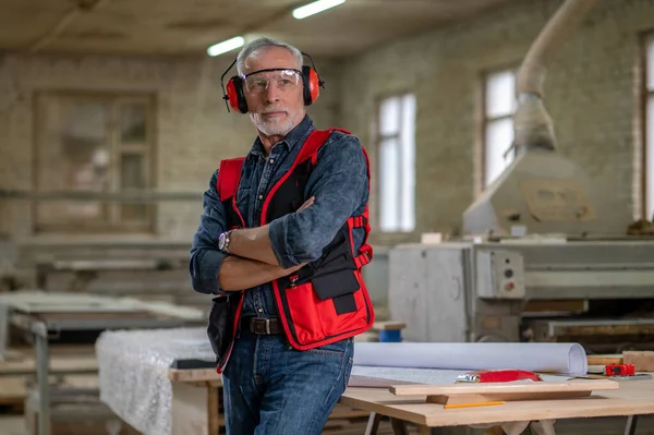 In a workshop. Mature man in eyeglasses and ear protector in a workshop