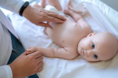 Tıbbi kontrol. Erkek çocuk doktoru bir bebeği muayene ediyor ve olaya dahil olmak istiyor.