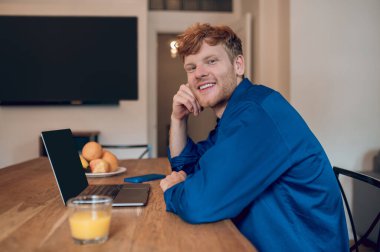 Morning at home. Ginger young man sitting at the table in the kithcen clipart