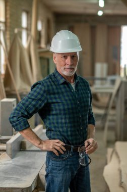 Kendine güveniyorsun. Olgun bir adam atölyede duruyor ve kendinden emin görünüyor.