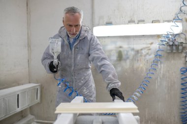 Ressam. Koruyucu giysiler içinde, odunları sprey silahla boyayan olgun bir adam.