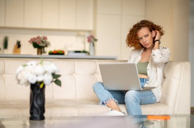Evden çalışıyorum. Kızıl saçlı genç kadın mutfakta oturuyor ve bir dizüstü bilgisayar üzerinde çalışıyor.