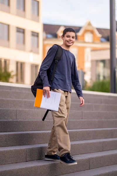 stock image Full-size portrait of a joyful teen with the textbook in one hand walking down the steps
