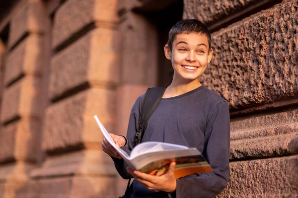 Waist-up portrait of a surprised adolescent with an open textbook in his hands looking into the distance
