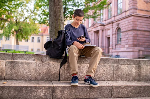 スマートフォンと本と落葉樹の下に座って幸せなかわいい学生の笑顔 — ストック写真