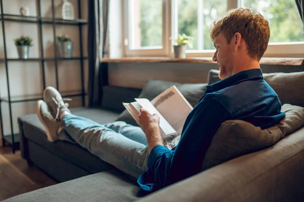 stock image Reading a book. A ginger man sitting at the window and reading a book