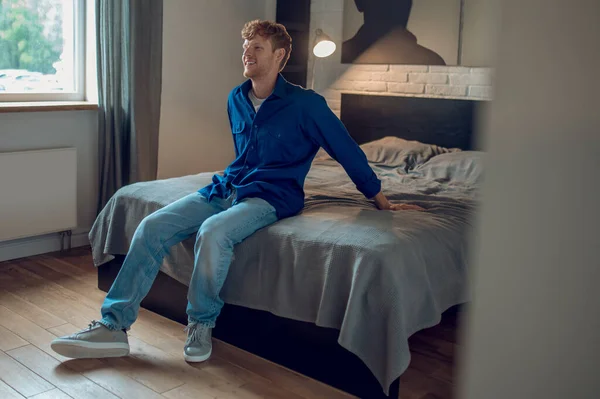 At home. A young man in dark-blue shirt sitting on the bed
