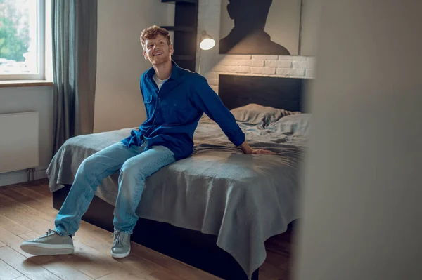 At home. A young man in dark-blue shirt sitting on the bed