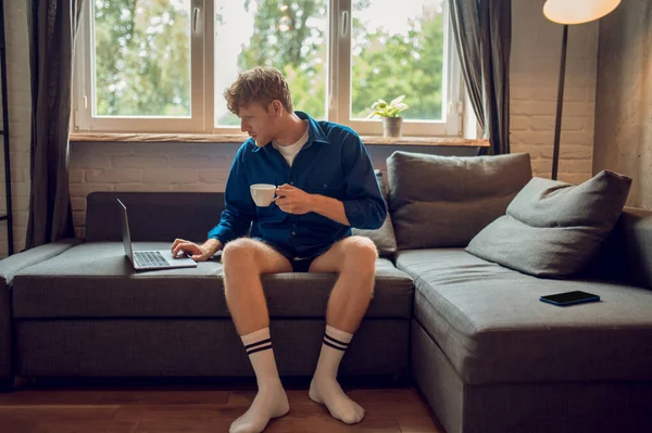 Morning. Young ginger man with a coffee mug in hand checking his email