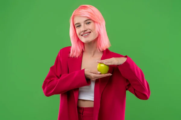 ウエストアップ肖像画の陽気な女の子とともに舌ピアスとブレース保持A緑のリンゴで彼女の手 — ストック写真