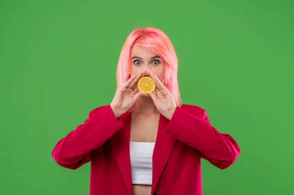 ウエストアップポートレートのいたずらな女の子とともにピンク色の髪ポージングとともにレモンの半分に緑の背景 — ストック写真