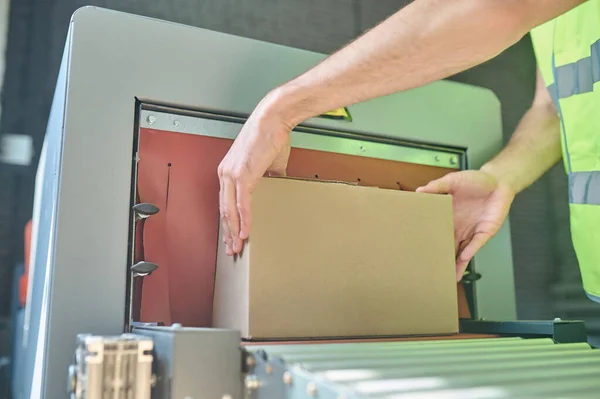 Stock image Cropped photo of a worker placing the cardboard box on the conveyor roller of the carton sealing machine