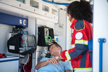 Ambulans hekimi sedyede yatan bir hastanın parmak ucuna nabız oksimetresini yerleştiriyor.