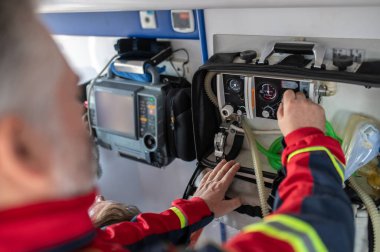 Solunum cihazının düğmesini çevirirken bir hastanın arkasında duran gri saçlı ambulans doktoru.
