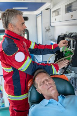 Solunum cihazının düğmesini çevirirken baygın bir insanın arkasında duran ciddi bir konsantre ambulans doktoru.