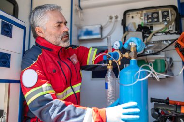 Oksijen tüpü vanasını çevirirken ambulansta oturan azot eldivenli ciddi odaklı doktor.