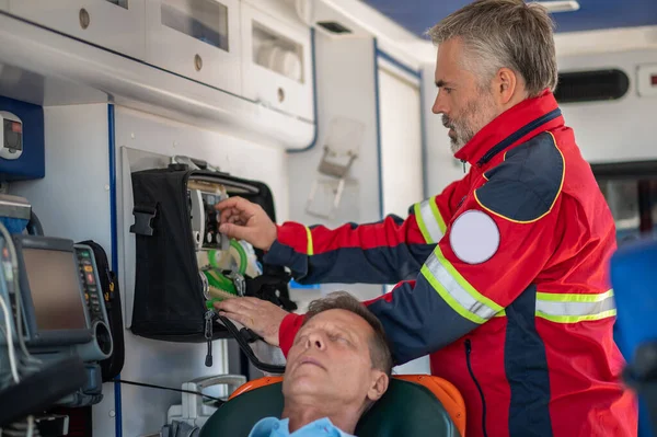 专心致志的辅助医务人员站在一个昏迷男子身后 转动呼吸装置上的旋钮 — 图库照片