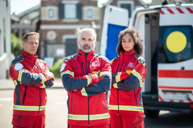 Ambulans minibüsünün yanında duran kırmızı üniformalı ciddi sağlık ekipleri.