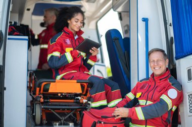 Neşeli orta yaşlı ambulans hekimi ve kırmızı üniformalı meslektaşları vardiyalarına hazırlanıyorlar.