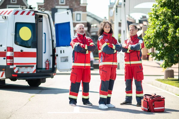 Ciddi bir ambulans doktorunun ve acil servis aracının yanında duran meslektaşlarının tam boy portresi.