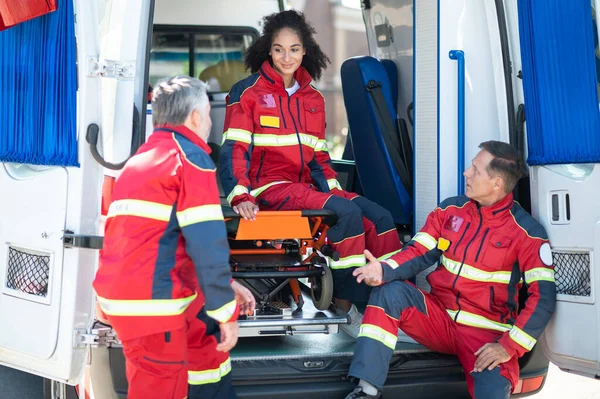 Nöjd Kvinnlig Sjukvårdare Sitter Båren Ambulansbilen Och Lyssnar Sina Kollegor — Stockfoto
