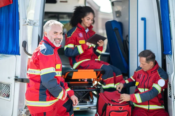 微笑着对站在他的同事旁边准备紧急医疗呼叫的成熟的医护人员感到高兴 — 图库照片